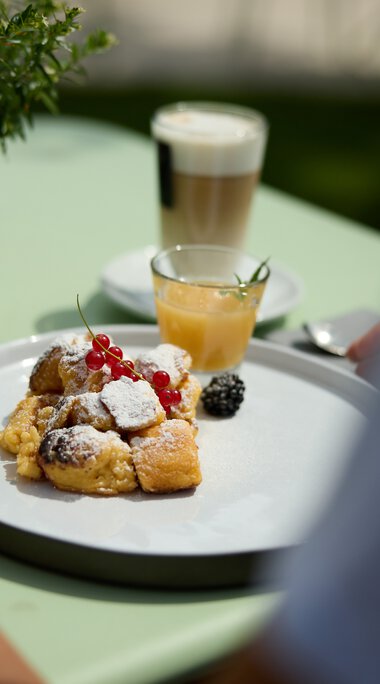 Ein Teller mit verschiedenen Frühstücksgebäcken, frischen Beeren und Puderzucker, auf einem grünen Tisch bei einer kulinarischen Wanderung im Kleinwalsertal. | © Kleinwalsertal Tourismus eGen • Fotograf: Oliver Farys