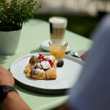 A plate with assorted breakfast pastries, fresh berries, and powdered sugar on a green table during a culinary hike in Kleinwalsertal. | © Kleinwalsertal Tourismus eGen • Photographer: Oliver Farys