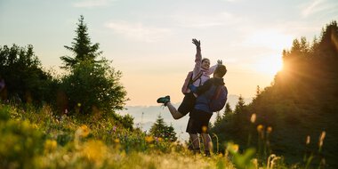 Ein Paar beim Wandern im Sonnenaufgang im Kleinwalsertal, umgeben von Natur und grünen Wiesen, mit Blick auf die aufgehende Sonne. | © Kleinwalsertal Tourismus eGen • Fotograf: Oliver Farys
