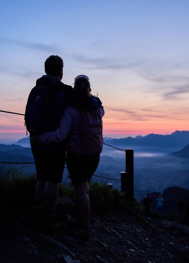 A couple watching the sunrise from a viewpoint in Kleinwalsertal overlooking the mountain landscape. | © Kleinwalsertal Tourismus eGen • Photographer: Oliver Farys