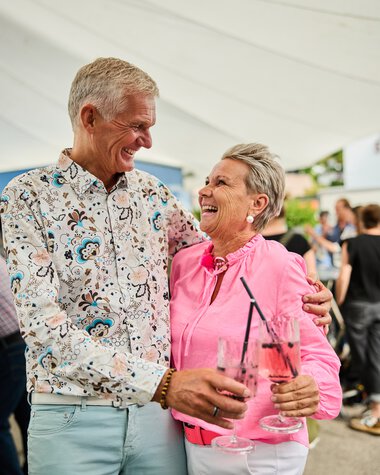 Lächelnde ältere Paare bei einem Sommerfest, die gemeinsam Getränke mit Strohhalmen halten und fröhlich miteinander sprechen. | © Kleinwalsertal Tourismus eGen • Fotograf: Oliver Farys