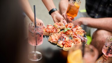 © Kleinwalsertal Tourismus eGen • Fotograf: Oliver Farys Menschen bei einem Sommer-Event im Kleinwalsertal, die Pizza servieren und Cocktails trinken. | © Kleinwalsertal Tourismus eGen • Fotograf: Oliver Farys