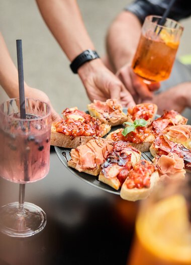 Menschen bei einem Sommer-Event im Kleinwalsertal, die Pizza servieren und Cocktails trinken. | © Kleinwalsertal Tourismus eGen • Fotograf: Oliver Farys