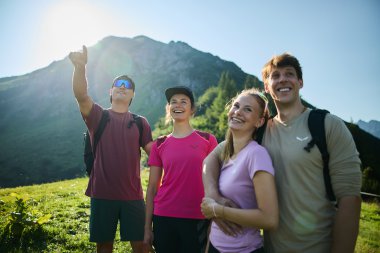 Vier junge Menschen beim Wandern in den Bergen, lachend und die Natur genießend, mit einem grünen Tal und Berg im Hintergrund. | © Kleinwalsertal Tourismus eGen • Fotograf: Oliver Farys