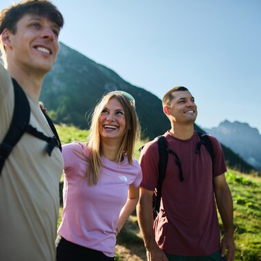 Drei junge Erwachsene beim Wandern in den Bergen, lachen und genießen die Natur im Kleinwalsertal. | ©  Kleinwalsertal Tourismus eGen • Fotograf: Oliver Farys