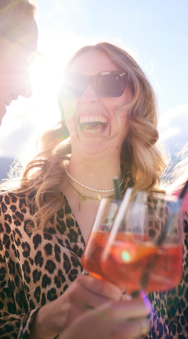 Drei lachende Frauen bei sommerlicher Lounge-Veranstaltung im Kleinwalsertal, trinken roséfarbene Getränke im Sonnenlicht. | © Kleinwalsertal Tourismus eGen • Fotograf: Oliver Farys