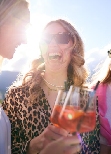 Drei lachende Frauen bei sommerlicher Lounge-Veranstaltung im Kleinwalsertal, trinken roséfarbene Getränke im Sonnenlicht. | © Kleinwalsertal Tourismus eGen • Fotograf: Oliver Farys