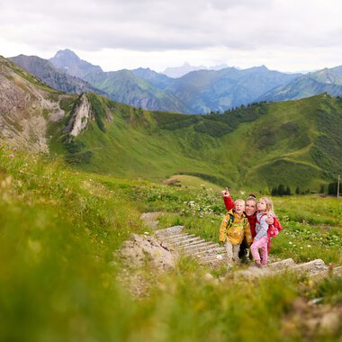 Children hiking in the mountains of Kleinwalsertal, surrounded by green hills and high peaks. | © Kleinwalsertal Tourismus eGen • Photographer: Oliver Farys
