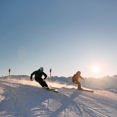 Zwei Skifahrer beim Rennen auf einer verschneiten Piste im Sonnenlicht in Kleinwalsertal, Österreich. | © Kleinwalsertal Tourismus eGen • Fotograf: Oliver Farys