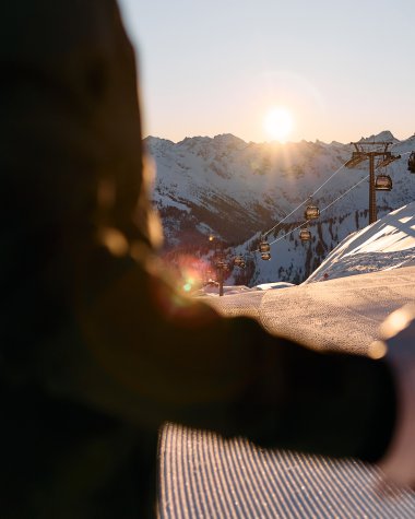 Ski-Alpin-Fahrer in der Abendsonne in Ifen, mit Skiberg und Sessellift im Hintergrund, bei Sonnenuntergang. | © Kleinwalsertal Tourismus eGen • Fotograf: Oliver Farys