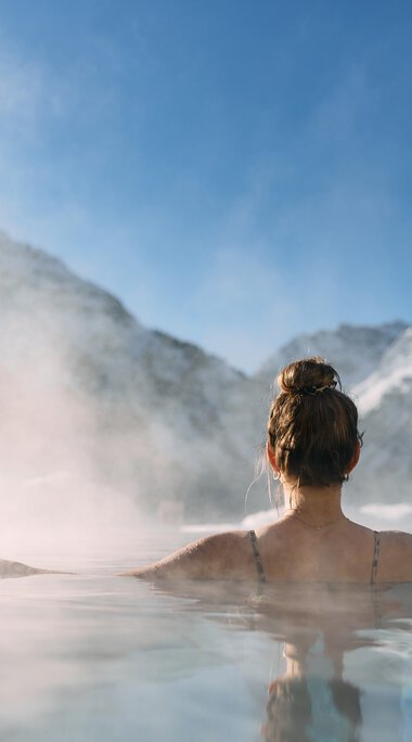 Frau entspannt in einem warmen schönen Spa mit Blick auf verschneite Berge im Kleinwalsertal, umgeben von Nebel und Natur. | © Kleinwalsertal Tourismus eGen • Fotograf: Oliver Farys