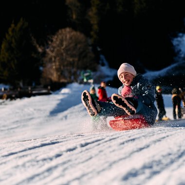 Ein Kind rodelnd im Schnee, Freude beim Winterspaß im Kleinwalsertal. | © Kleinwalsertal Tourismus eGen • Fotograf: Oliver Farys