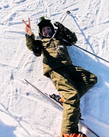 Kind beim Skifahren im Kleinwalsertal, lächelnd und das Peace-Zeichen machend, in Winterkleidung auf Schneepiste. | © Kleinwalsertal Tourismus eGen • Fotograf: Oliver Farys