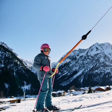 Ein Kind beim Skifahren im Winter, umgeben von verschneiten Bergen und klarer Himmel | © Kleinwalsertal Tourismus eGen • Fotograf: Oliver Farys