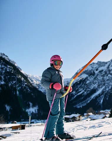 Ein Kind beim Skifahren im Winter, umgeben von verschneiten Bergen und klarer Himmel | © Kleinwalsertal Tourismus eGen • Fotograf: Oliver Farys