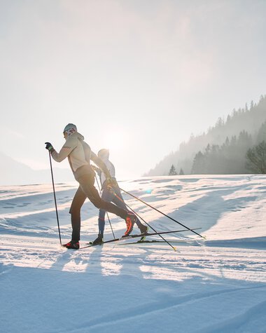 Zwei Skifahrer beim klassischen Langlauf auf der Schwarzwasserloipe im Kleinwalsertal bei Sonnenaufgang. | © Kleinwalsertal Tourismus eGen • Fotograf: Oliver Farys