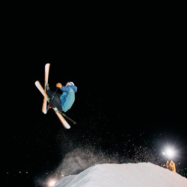 Skifahrer bei Nachtskifahren im Kleinwalsertal, jongliert mit Skiern in der Luft gegen den dunklen Nachthimmel. | © Kleinwalsertal Tourismus eGen • Fotograf: Oliver Farys