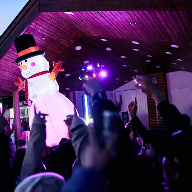 Große Schneemänner-Dekoration bei einer Winterveranstaltung in Kleinwalsertal, beleuchtet mit bunten Lichteffekten, während Kinder teilnehmen. | © Kleinwalsertal Tourismus eGen • Fotograf: Oliver Farys