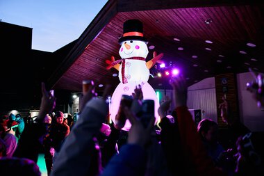 Große Schneemänner-Deko auf einer Winterveranstaltung im Kleinwalsertal, umgeben von Kindern, die zum Schnee-Fest jubeln. | © Kleinwalsertal Tourismus eGen • Fotograf: Oliver Farys
