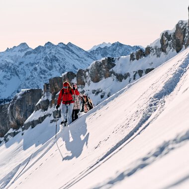 Two snowshoe hikers ascend a snowy mountain slope with rugged peaks in the background in Kleinwalsertal. | © Kleinwalsertal Tourismus eGen • Photographer: Oliver Farys