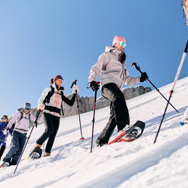Mehrere Personen bei einer Schneeschuhwanderung im verschneiten Gebirge, unterwegs in winterlicher Kleidung mit Skistöcken. | © Kleinwalsertal Tourismus eGen • Fotograf: Oliver Farys