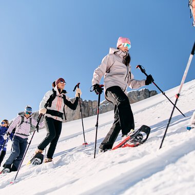 Group of people snowshoeing on a snowy mountain, dressed in winter gear with trekking poles. | © Kleinwalsertal Tourismus eGen • Photographer: Oliver Farys