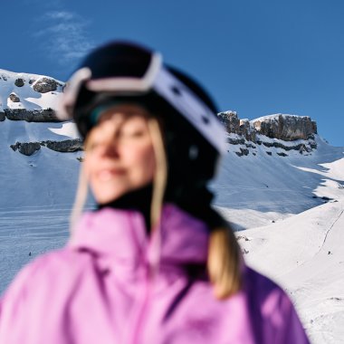 Verweanyte Person mit Ski- oder Snowboardhelm im Winterurlaub in den Bergen, Schnee und Felsen im Hintergrund, blauer Himmel. | © Kleinwalsertal Tourismus eGen • Fotograf: Oliver Farys