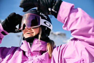 Junge Frau beim Skifahren im Winter, trägt pinke Skimode, Helm und Skibrille, lächelt | © Kleinwalsertal Tourismus eGen • Fotograf: Oliver Farys