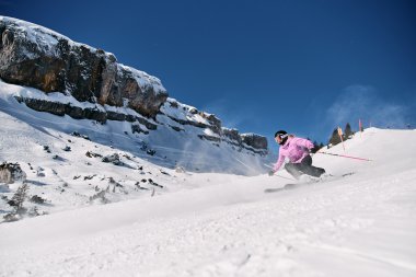 Skifahrerin beim Abfahrt auf einer verschneiten Piste im Kleinwalsertal, mit Felsen im Hintergrund und klarem blauen Himmel. | © Kleinwalsertal Tourismus eGen • Fotograf: Oliver Farys