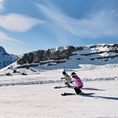 Zwei Kinder beim Skifahren auf winterlicher Piste vor einer Berglandschaft im Kleinwalsertal, mit blauen Himmel und Wolken. | © Kleinwalsertal Tourismus eGen • Fotograf: Oliver Farys