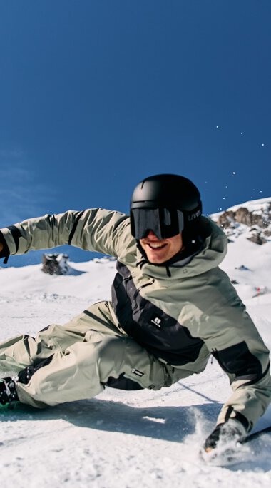 Skifahrer in einem weißen Skianzug trägt einen schwarzen Helm und fährt im Tiefschnee bei klarem Himmel im Skigebiet Ifen. | ©  Kleinwalsertal Tourismus eGen • Fotograf: Oliver Farys