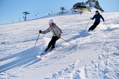 Zwei Skifahrer in Winterkleidung auf einer verschneiten Piste beim Abfahren am Kanzelwand. Im Hintergrund sieht man Bergstrukturen und Skilifte. | © Kleinwalsertal Tourismus eGen • Fotograf: Oliver Farys