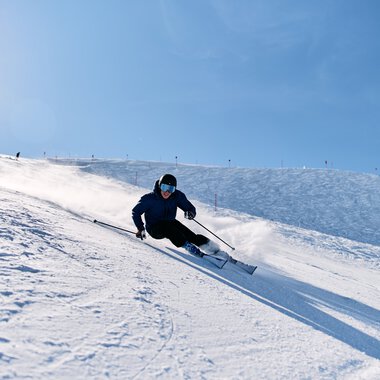 Ein Skifahrer in dunkler Kleidung und mit Skibrille fährt an steiler Piste im Schneeterrain ab. | © Kleinwalsertal Tourismus eGen • Fotograf: Oliver Farys