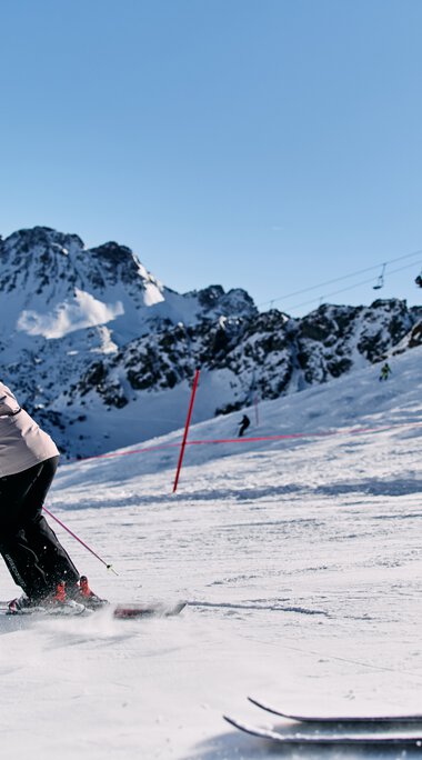 Zwei Skifahrer beim Abfahrtski auf einer verschneiten Piste in den Bergen, im Hintergrund schneebedeckte Gipfel und klarer blauer Himmel. | © Kleinwalsertal Tourismus eGen • Fotograf: Oliver Farys