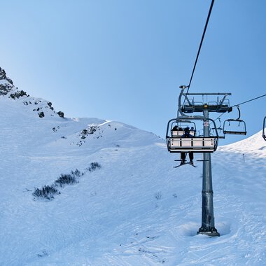 Ski lift in snowy mountain landscape with blue sky at Kleinwalsertal in winter. | © Kleinwalsertal Tourismus eGen • Photographer: Oliver Farys