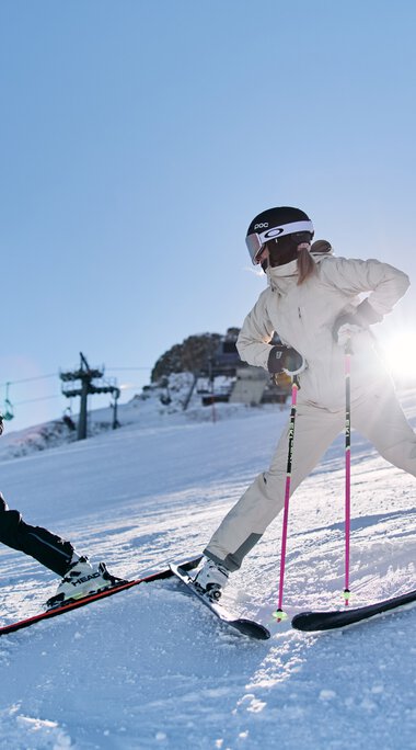 Zwei Kinder beim Skifahren am Kanzelwand in Kleinwalsertal, Sonnenlicht im Hintergrund, winterliche Berglandschaft. | © Kleinwalsertal Tourismus eGen • Fotograf: Oliver Farys