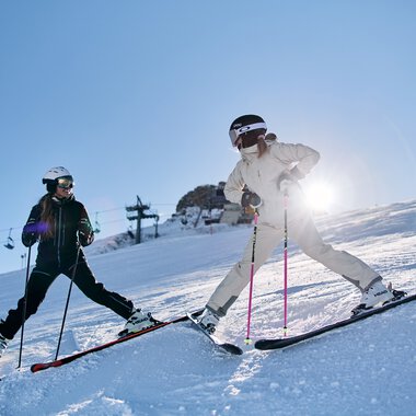 Zwei Kinder beim Skifahren am Kanzelwand in Kleinwalsertal, Sonnenlicht im Hintergrund, winterliche Berglandschaft. | © Kleinwalsertal Tourismus eGen • Fotograf: Oliver Farys