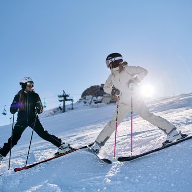 Zwei Kinder beim Skifahren am Kanzelwand in Kleinwalsertal, Sonnenlicht im Hintergrund, winterliche Berglandschaft. | © Kleinwalsertal Tourismus eGen • Fotograf: Oliver Farys