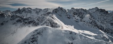 Schneebedeckte Berggipfel und -hänge unter einem bewölkten Himmel in einer winterlichen Landschaft.