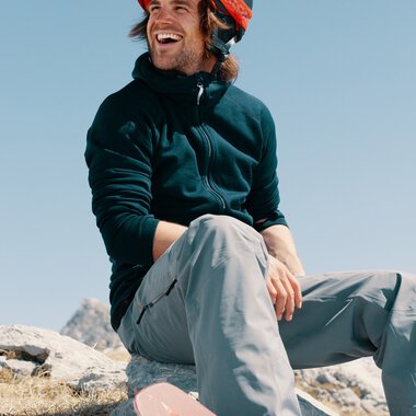 Young man with a helmet and gloves, smiling in the snow, sitting in front of a ski lift | © Kleinwalsertal Tourismus eGen • Photographer: Distillery