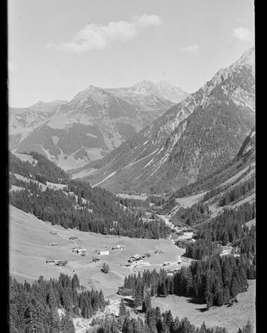 Schöne Berglandschaft im Tal mit kleinen Bauernhöfen, umgeben von hohen Gipfeln, im historischen Schwarz-Weiß-Foto. | © Kleinwalsertal Tourismus eGen • Karl Marx Kessler Archiv