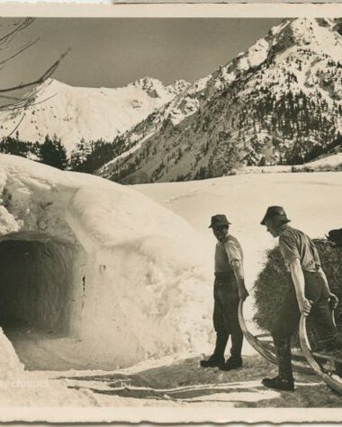 Zwei Männer vor einem Schneeloch in einer verschneiten Berglandschaft, historische Fotografie. | © Kleinwalsertal Tourismus eGen • Stefan Heim