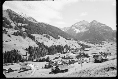 Historisches Schwarz-Weiß-Foto des Dorfes Hirschegg im Kleinwalsertal mit Kirche, umgeben von Bergen und Wiesen in den Alpen. | © Kleinwalsertal Tourismus eGen • Karl Marx Kessler Archiv
