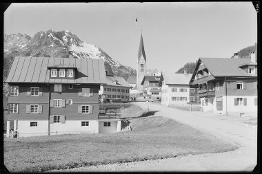 Historisches Schwarz-Weiß-Foto des Dorfes Mittelberg mit Kirche und Bergen im Hintergrund. | © Kleinwalsertal Tourismus eGen • Karl Marx Kessler Archiv