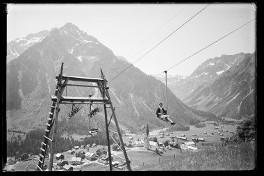 Historisches Foto eines Skiliftantriebs in einem Tal, mit Bergen im Hintergrund und kleinen Gebäuden im Vordergrund. | © Kleinwalsertal Tourismus eGen • Karl Marx Kessler Archiv