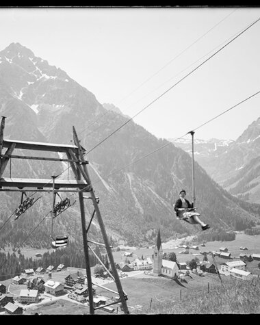 Historisches Foto eines Skiliftantriebs in einem Tal, mit Bergen im Hintergrund und kleinen Gebäuden im Vordergrund. | © Kleinwalsertal Tourismus eGen • Karl Marx Kessler Archiv
