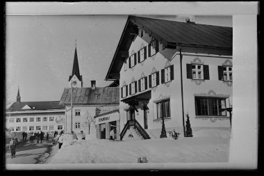 Historisches Schwarz-Weiß-Foto eines Schuh- und Modehauses im Zentrum von Riezlern, mit einem Mann und einer Frau vor dem Geschäft, im Schnee. | © Kleinwalsertal Tourismus eGen • Karl Marx Kessler Archiv