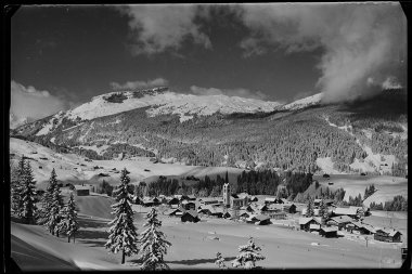 Schöne schwarze und weiße Fotografie von Riezlern auf 1100 m Höhe, umgeben von verschneiten Bergen und Tannen im Winter. | © Kleinwalsertal Tourismus eGen • Karl Marx Kessler Archiv
