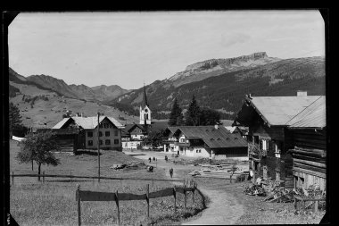 Historisches Foto von Riezlern, mit Kirchturm im Zentrum, umliegende Gebäude und Berge im Hintergrund. | © Kleinwalsertal Tourismus eGen • Karl Marx Kessler Archiv