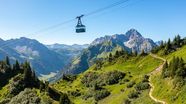 © Oberstdorf · Kleinwalsertal Bergbahnen Bergbahn fährt über grüne Hänge und Berge im Kleinwalsertal, mit einem klaren blauen Himmel im Hintergrund. | © Oberstdorf · Kleinwalsertal Bergbahnen